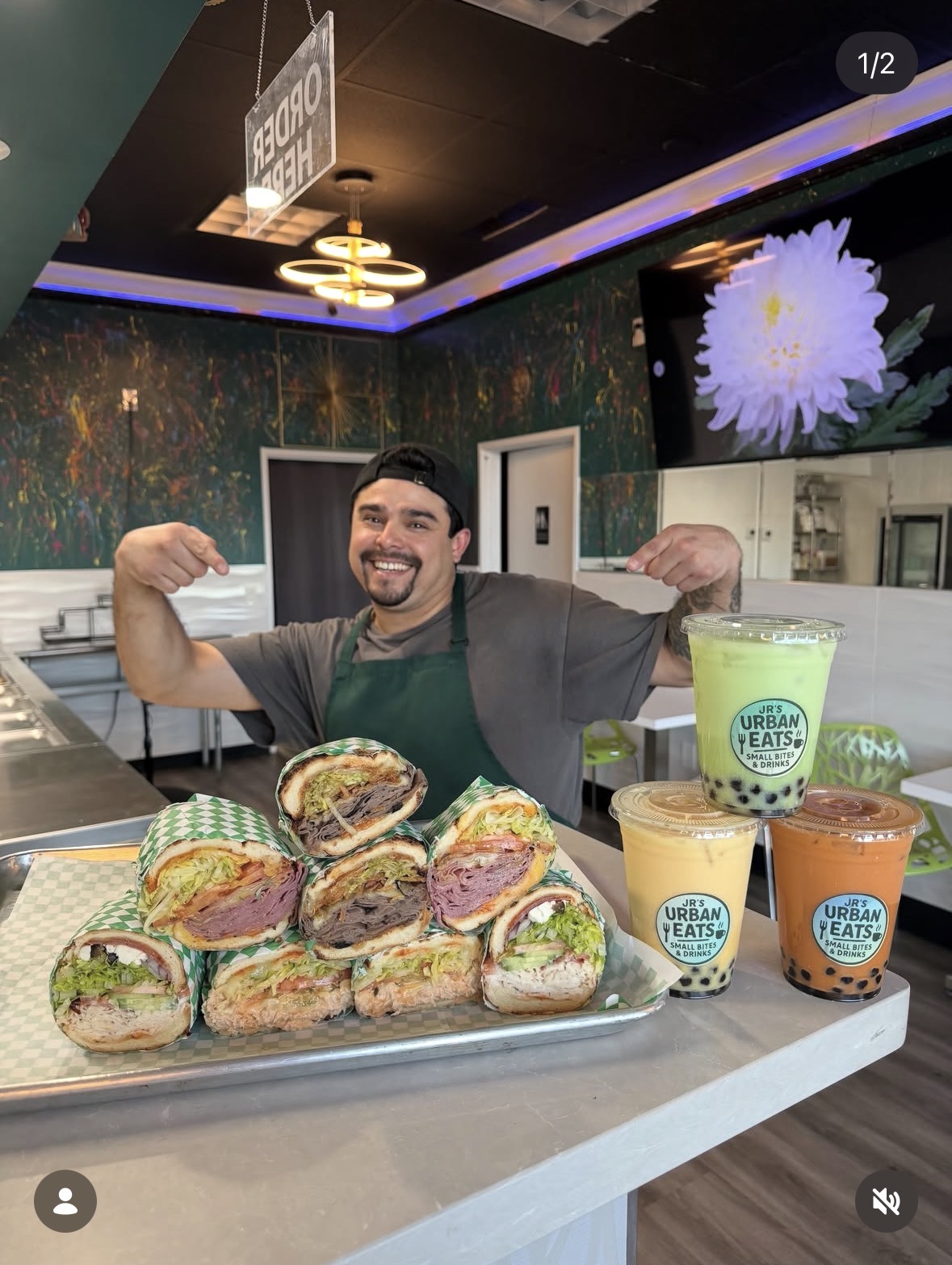 Jr's Urban Eats owner proudly presenting a stack of fresh sandwiches and three colorful boba drinks in-store